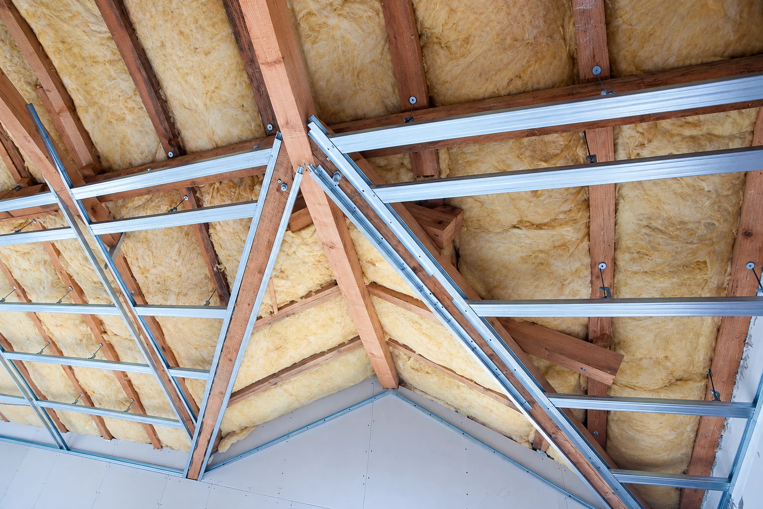 Yellow fiberglass batts fill the spaces between attic rafters and metal framing channels.