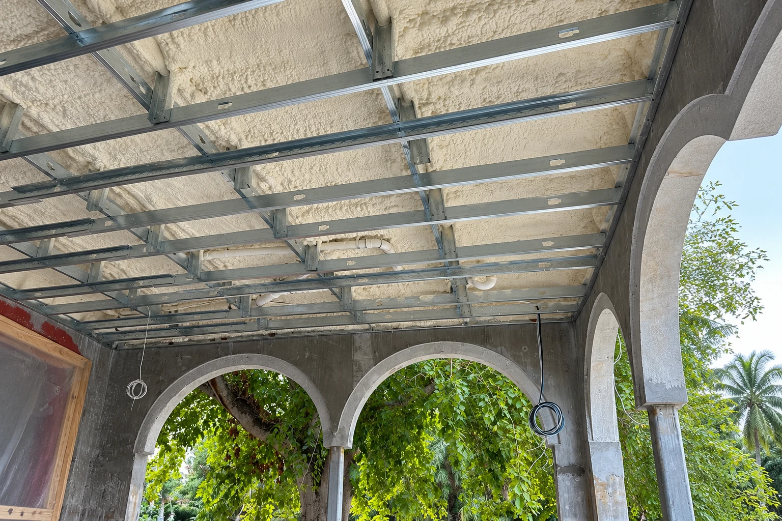Open porch ceiling coated with cream-colored spray foam behind a grid of metal framing.