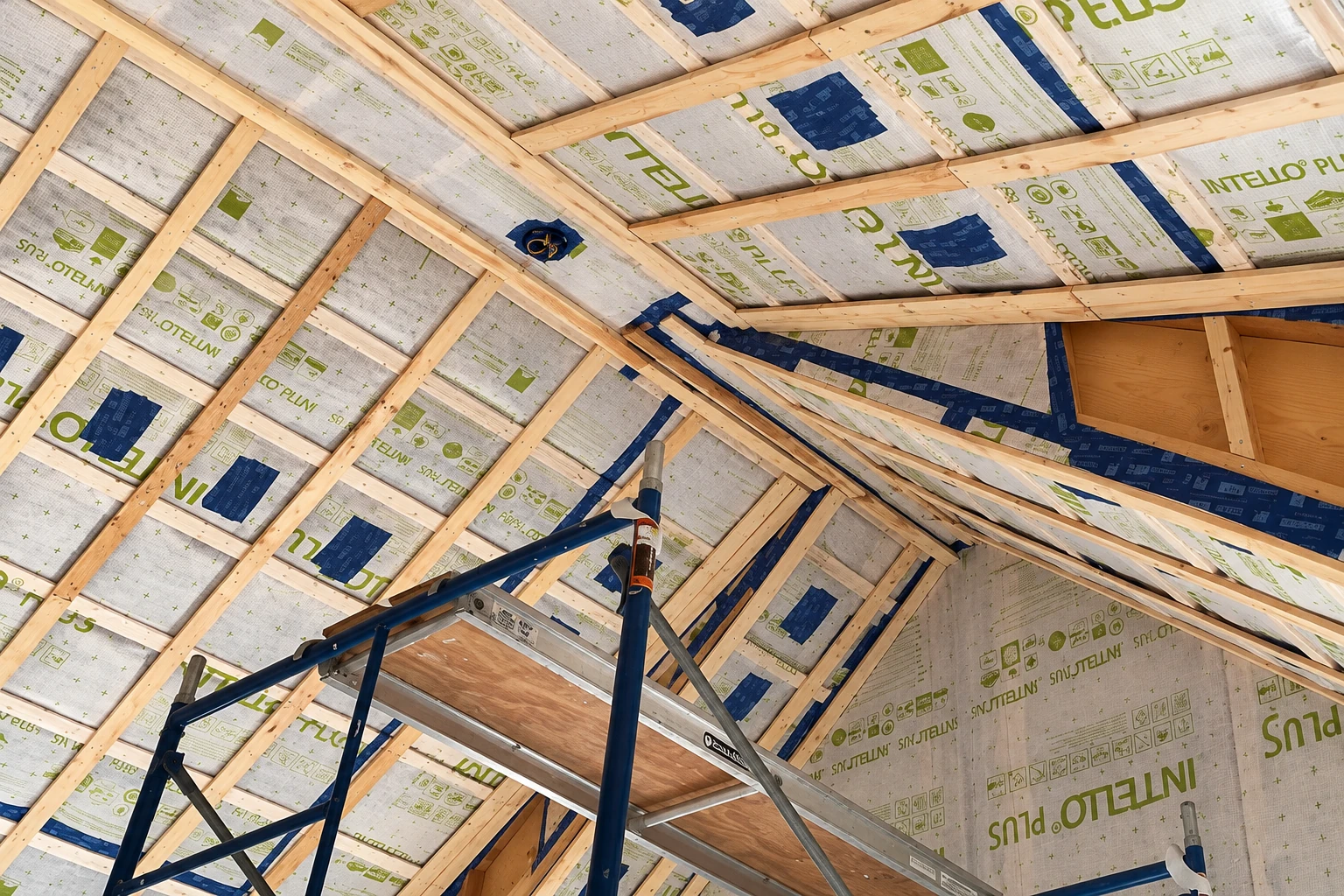Foil-faced vapor barrier covers a wooden roof frame, with seams taped in blue and green.